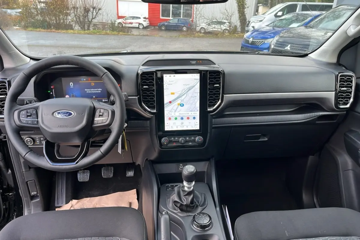 Vue intérieure avant du Ford Ranger noir shadow 2025, avec tableau de bord moderne et écran tactile vertical central.