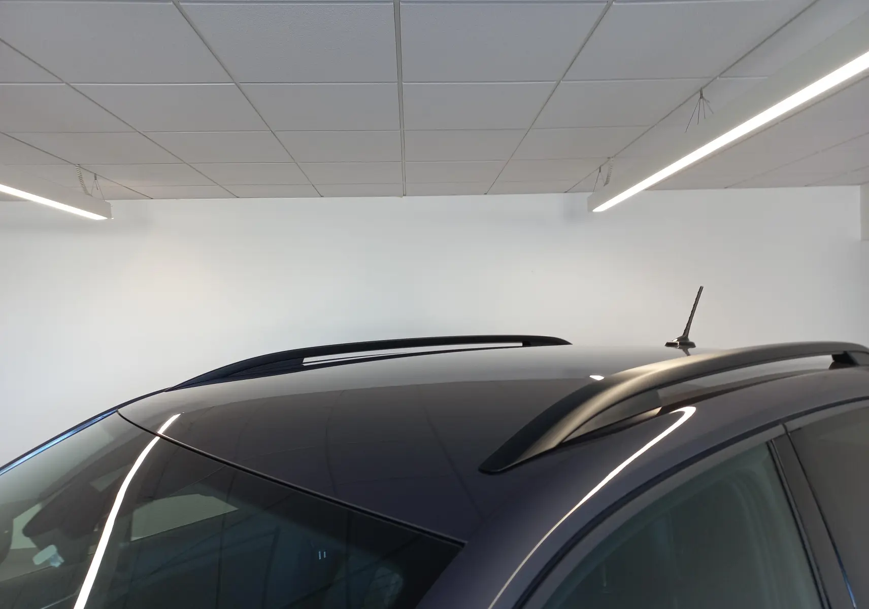 Toit panoramique et barres de toit noires sur Volkswagen T-Cross gris cendré, vue rapprochée en intérieur.