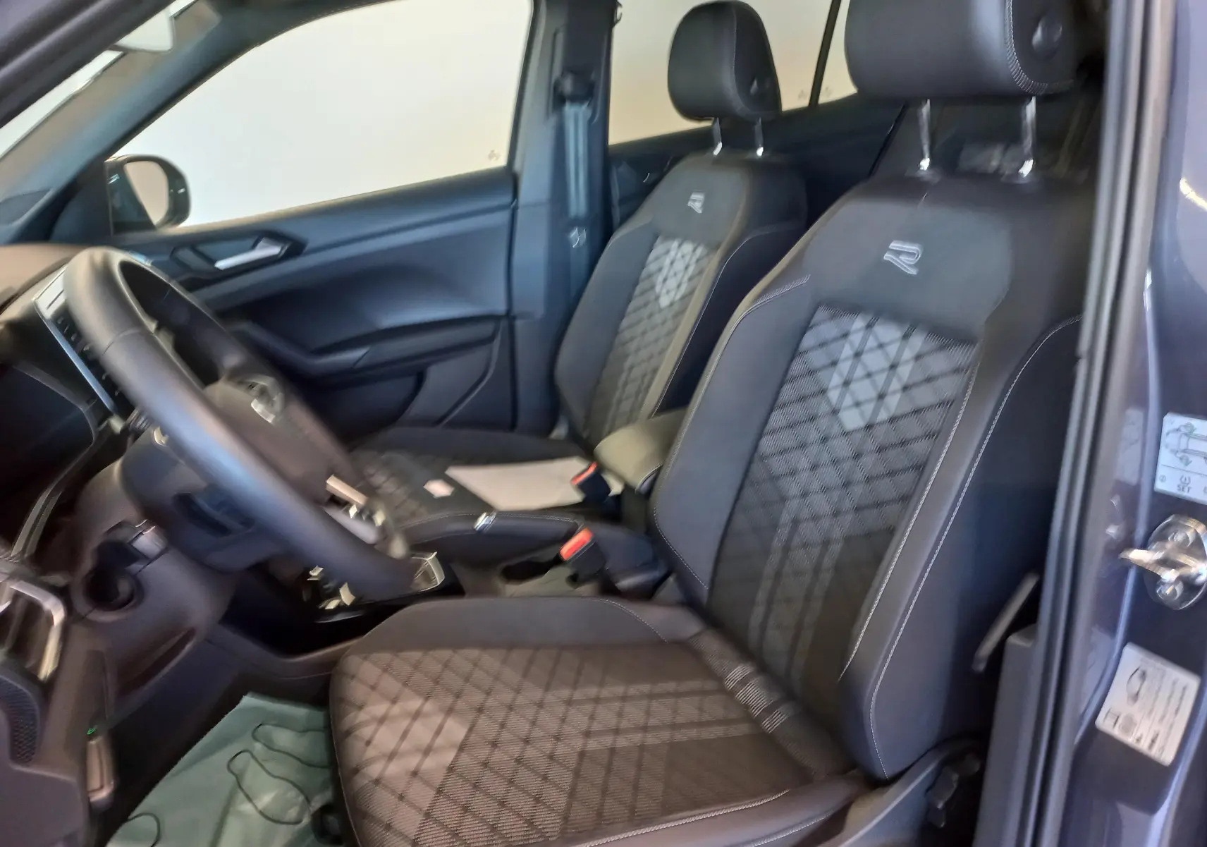 Vue intérieure côté conducteur du Volkswagen T-Cross 1.0 TSI R-Line Edition avec sièges noirs à surpiqûres et logo R brodé.