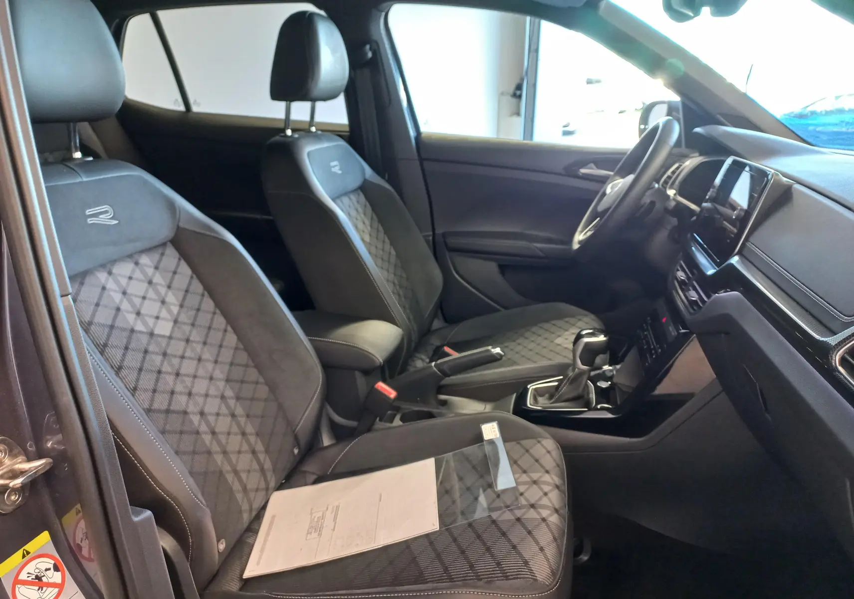Vue intérieure côté gauche du Volkswagen T-Cross gris cendre, sièges R-Line avec surpiqûres losanges et tableau de bord moderne.