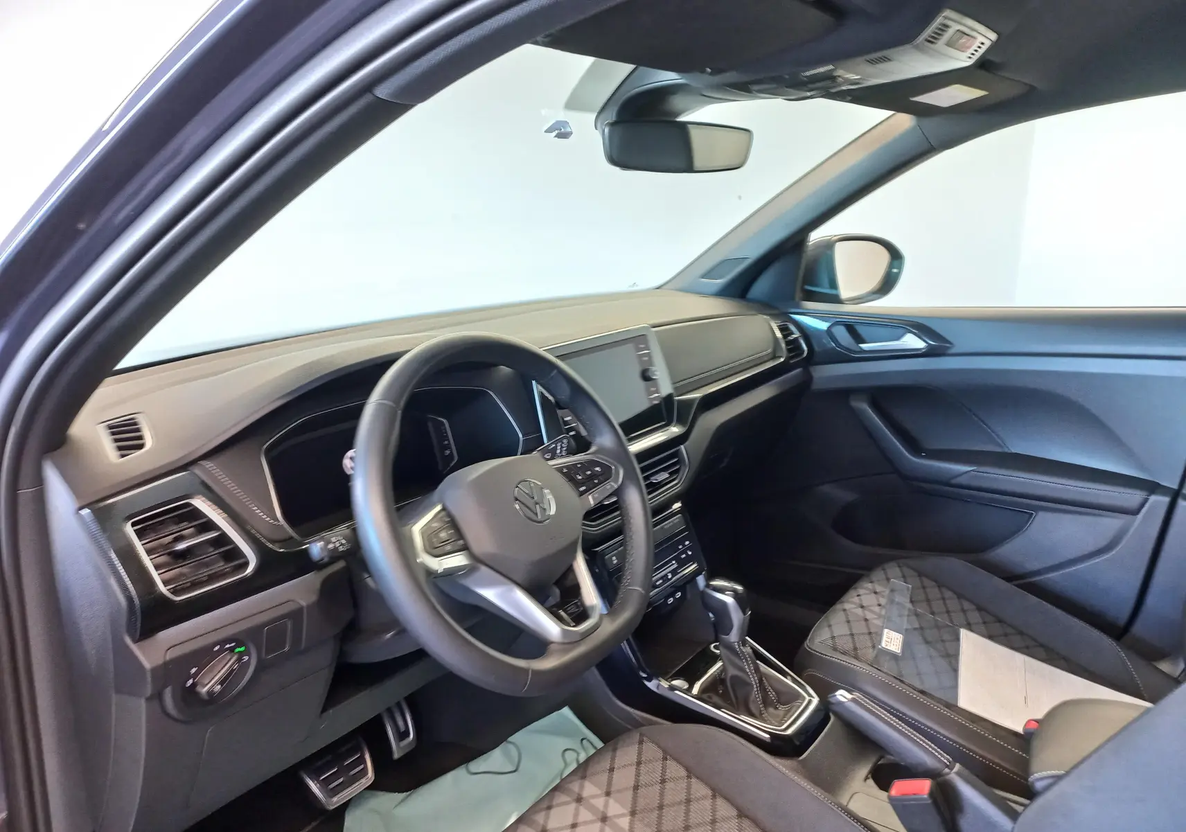 Vue intérieure côté conducteur du Volkswagen T-Cross 2025, tableau de bord noir avec volant multifonction et sellerie tissu à motifs.