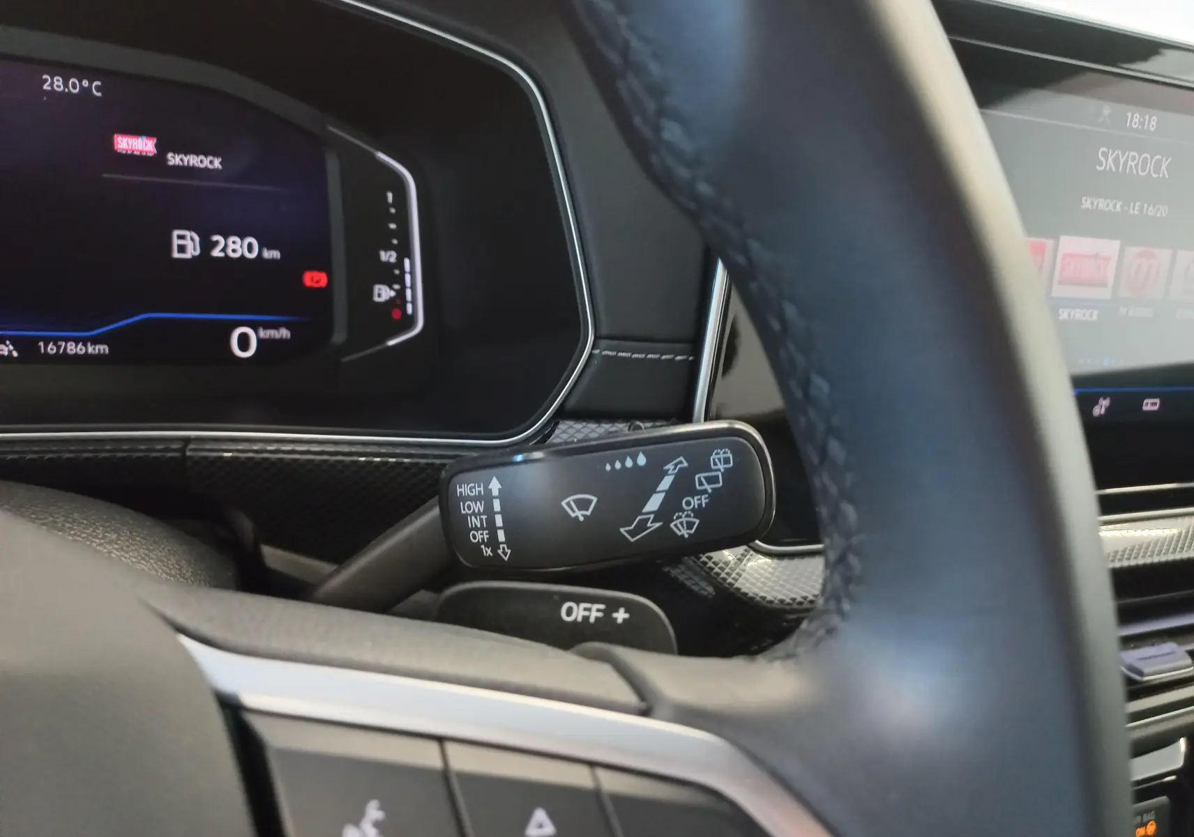 Vue rapprochée du commodo d’essuie-glace derrière le volant d’un Volkswagen T-Cross gris cendré, tableau de bord numérique en arrière-plan.