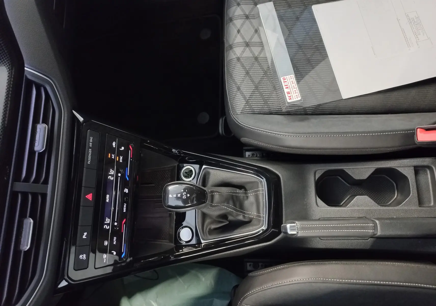 Vue intérieure centrée sur la console centrale du Volkswagen T-Cross 2025, avec levier de vitesse DSG et sièges tissu gris.