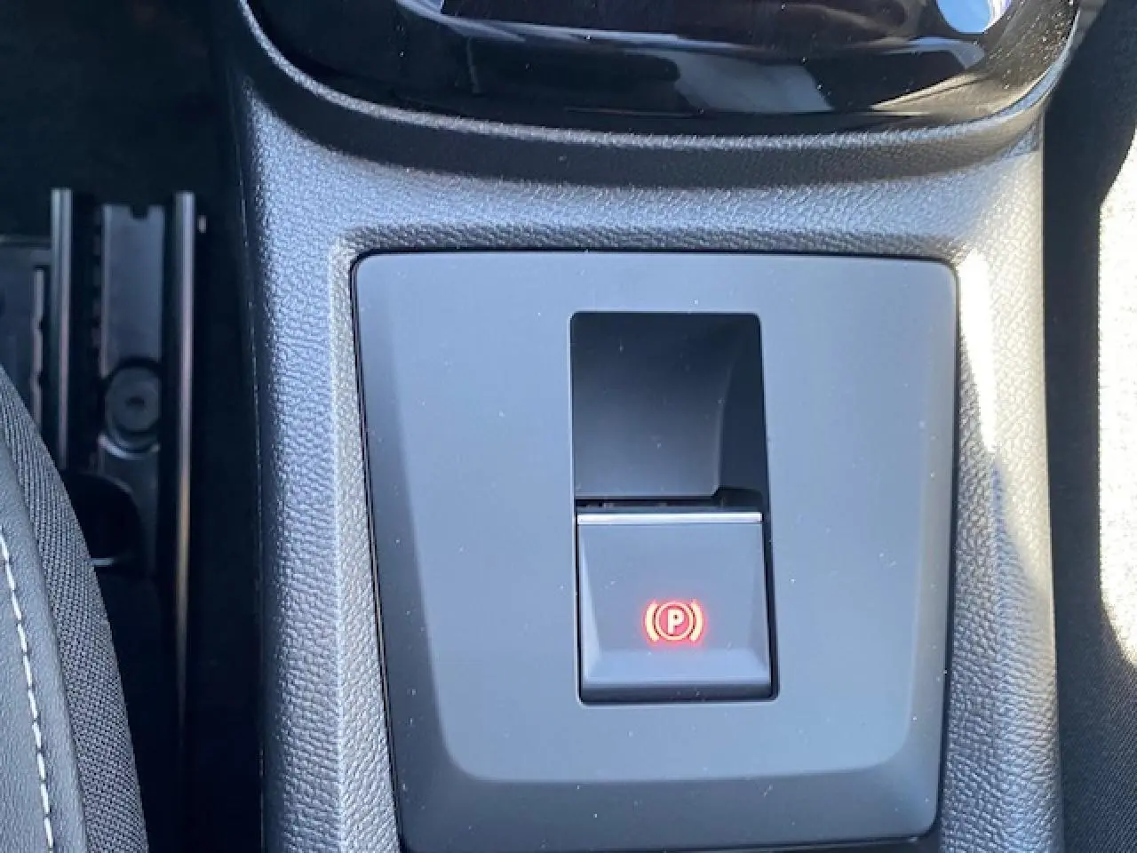 Gros plan sur le frein de stationnement électrique avec témoin rouge dans la console centrale d'une Citroën C3 Aircross gris Mercury.