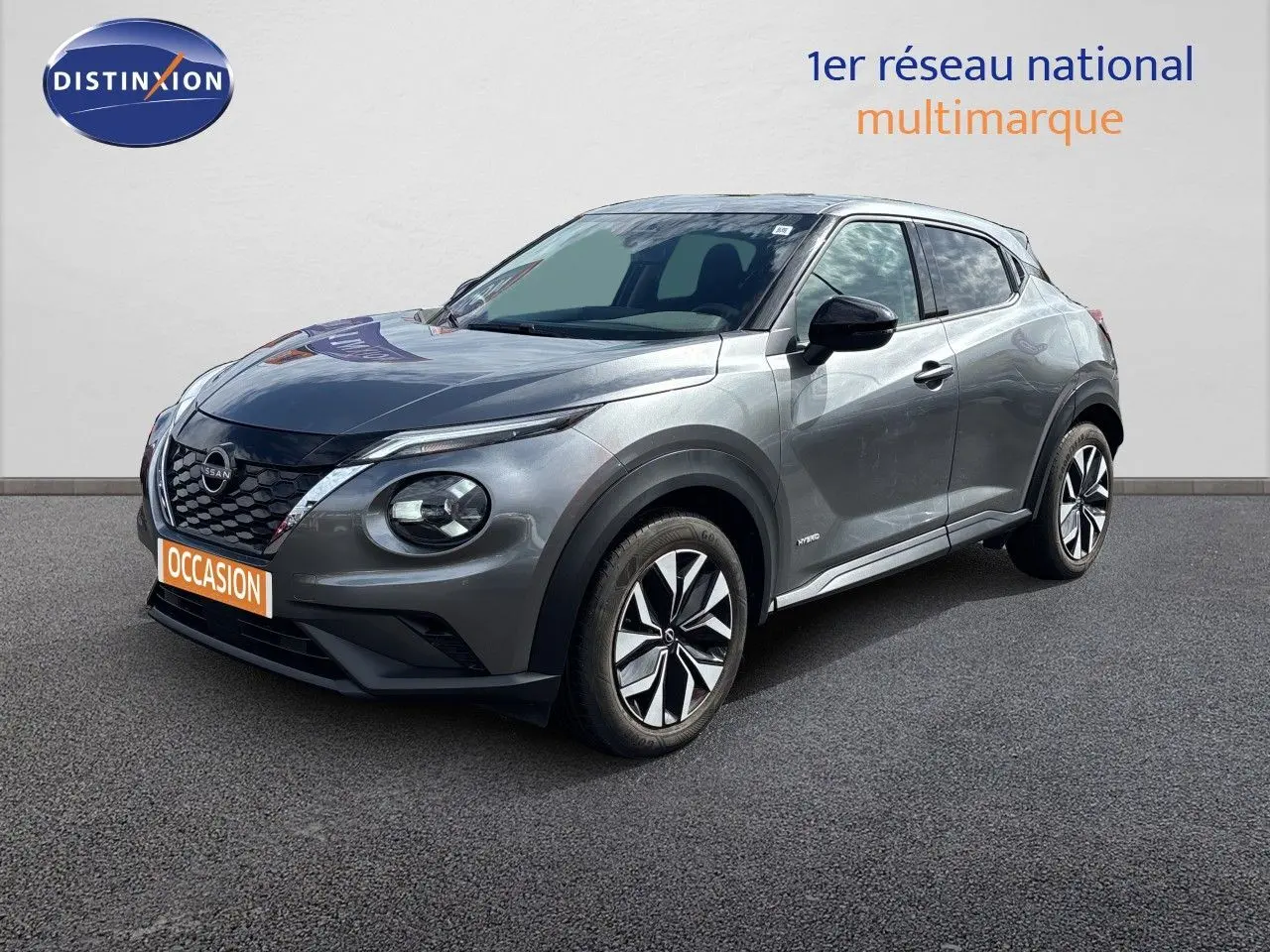 Nissan Juke Hybrid gris squale métal en 3/4 avant droit, avec jantes modernes et calandre noire distinctive.