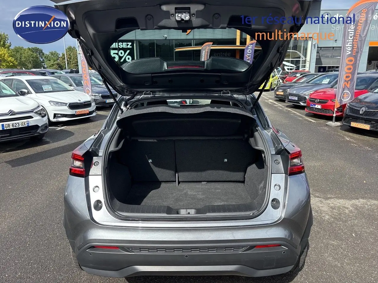 Vue arrière du Nissan Juke Hybrid 143ch Business Edition gris squale métal avec coffre ouvert sur parking extérieur.
