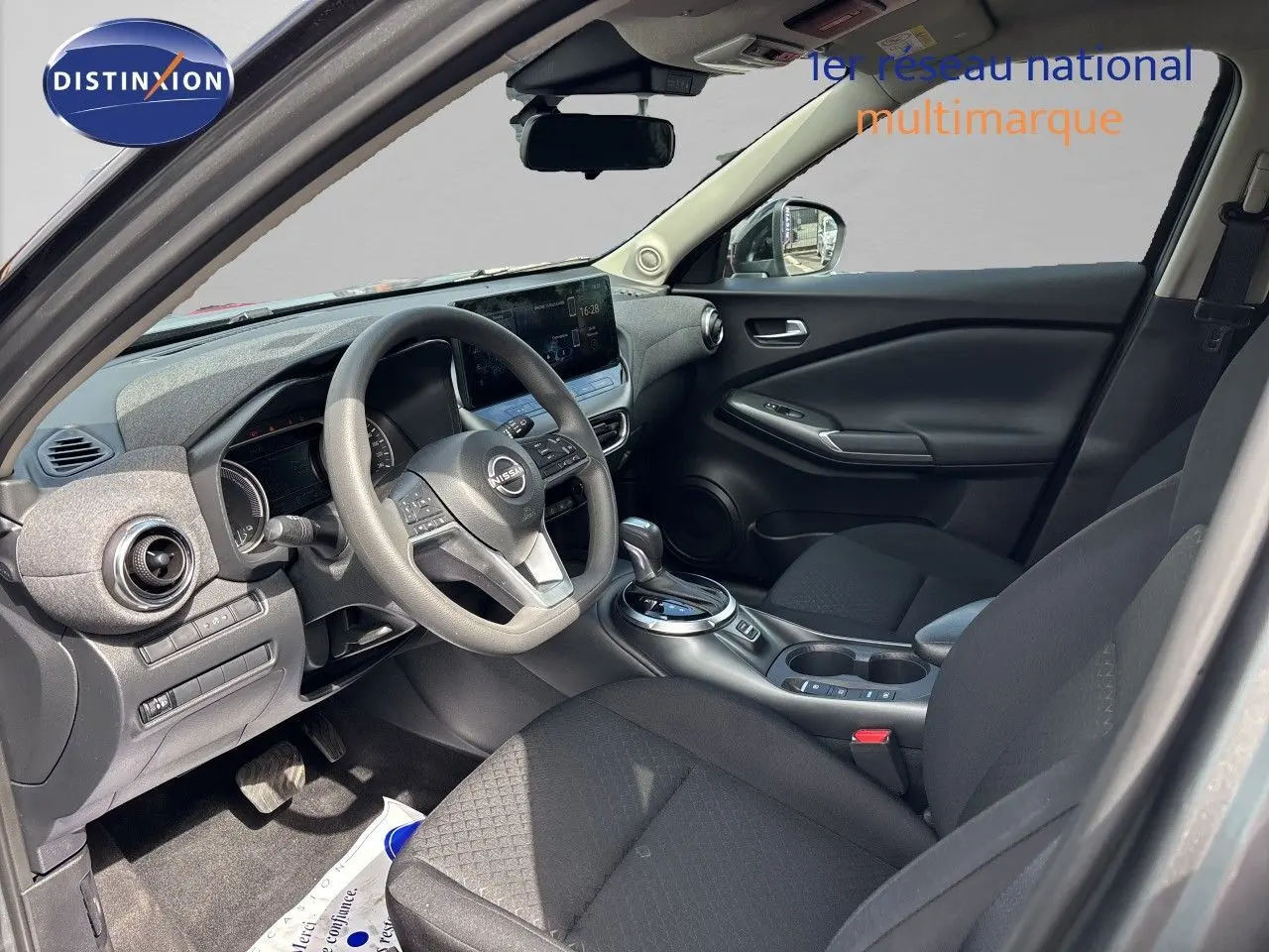Vue intérieure avant du tableau de bord et volant du Nissan Juke Hybrid 2024 avec écran tactile central et finition noire.