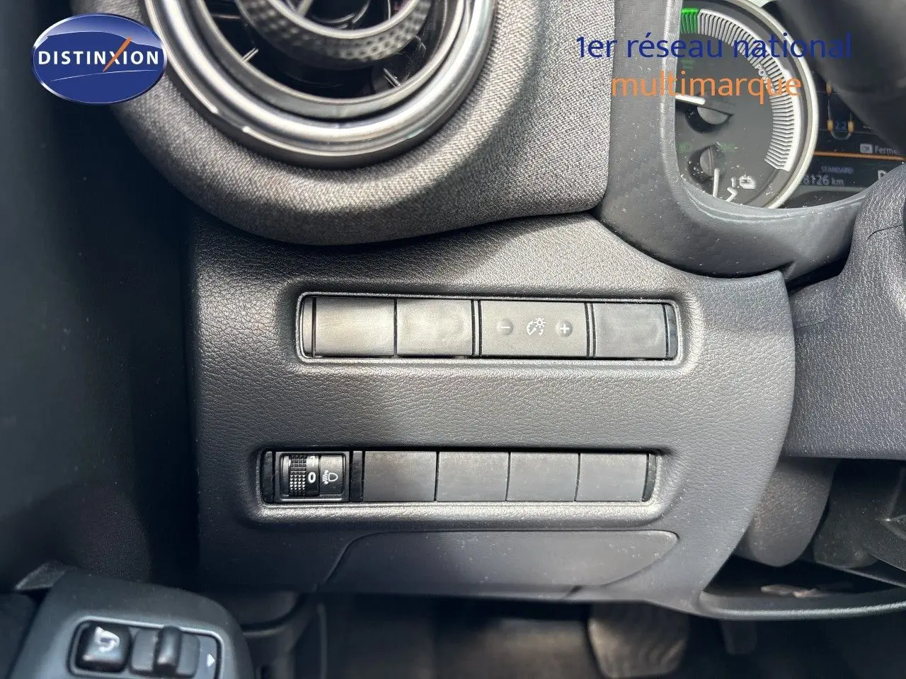 Gros plan sur le commodo d’éclairage à gauche du volant du Nissan Juke Hybrid gris, avec tableau de bord numérique en arrière-plan.