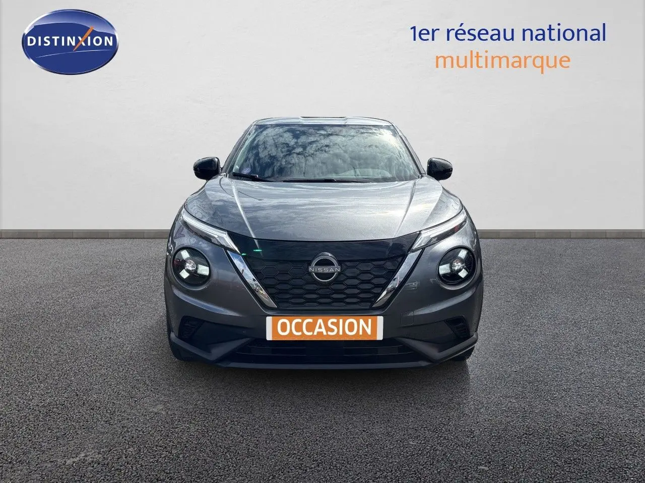 Vue frontale d'un Nissan Juke Hybrid 143ch Business Edition gris squale métal avec calandre noire et phares ronds LED.