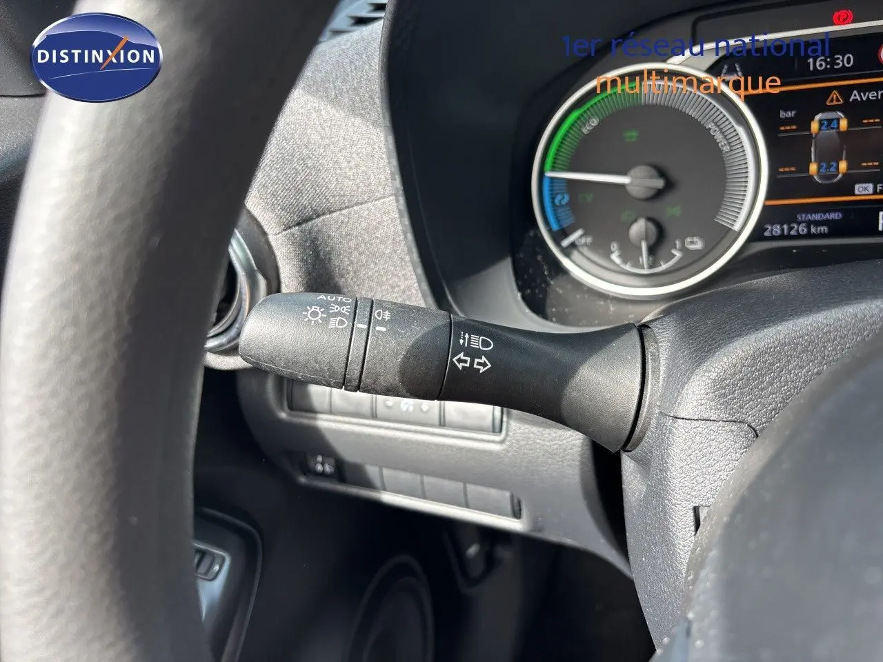 Gros plan sur les commandes au volant noir du Nissan Juke Hybrid 2024, avec tableau de bord et aérateur circulaire en arrière-plan.