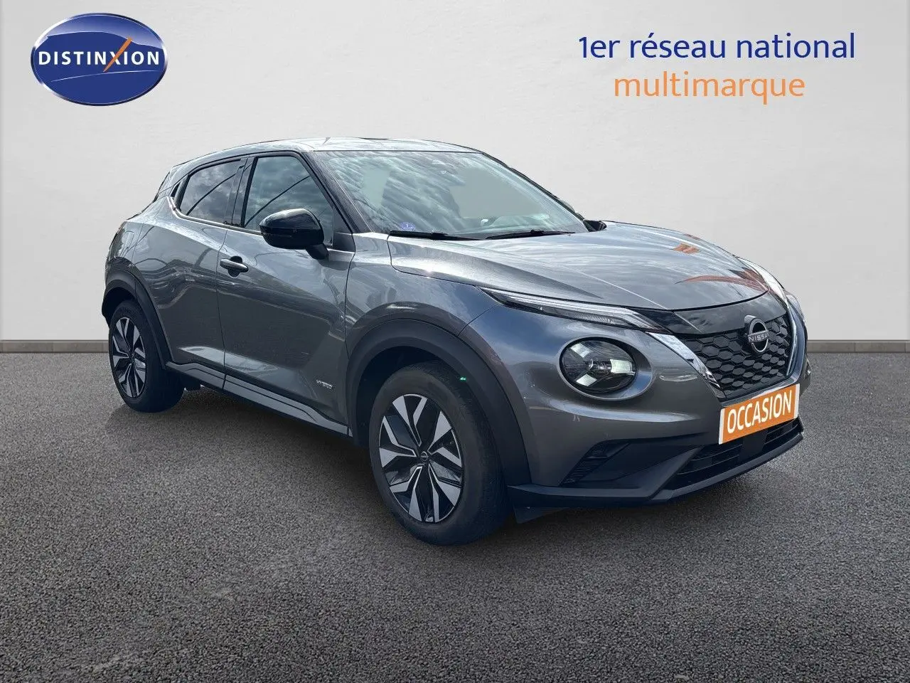 Nissan Juke Hybrid gris squale métal en 3/4 avant droit, avec calandre noire et jantes stylisées.