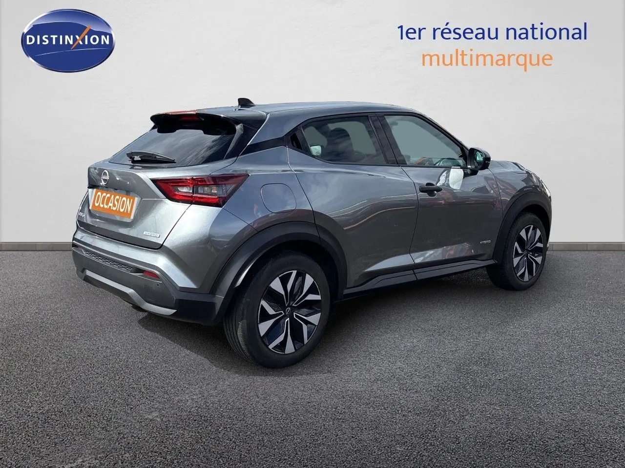 Nissan Juke Hybrid gris squale métal vu en 3/4 arrière droit, avec jantes noires et toit noir contrastant.