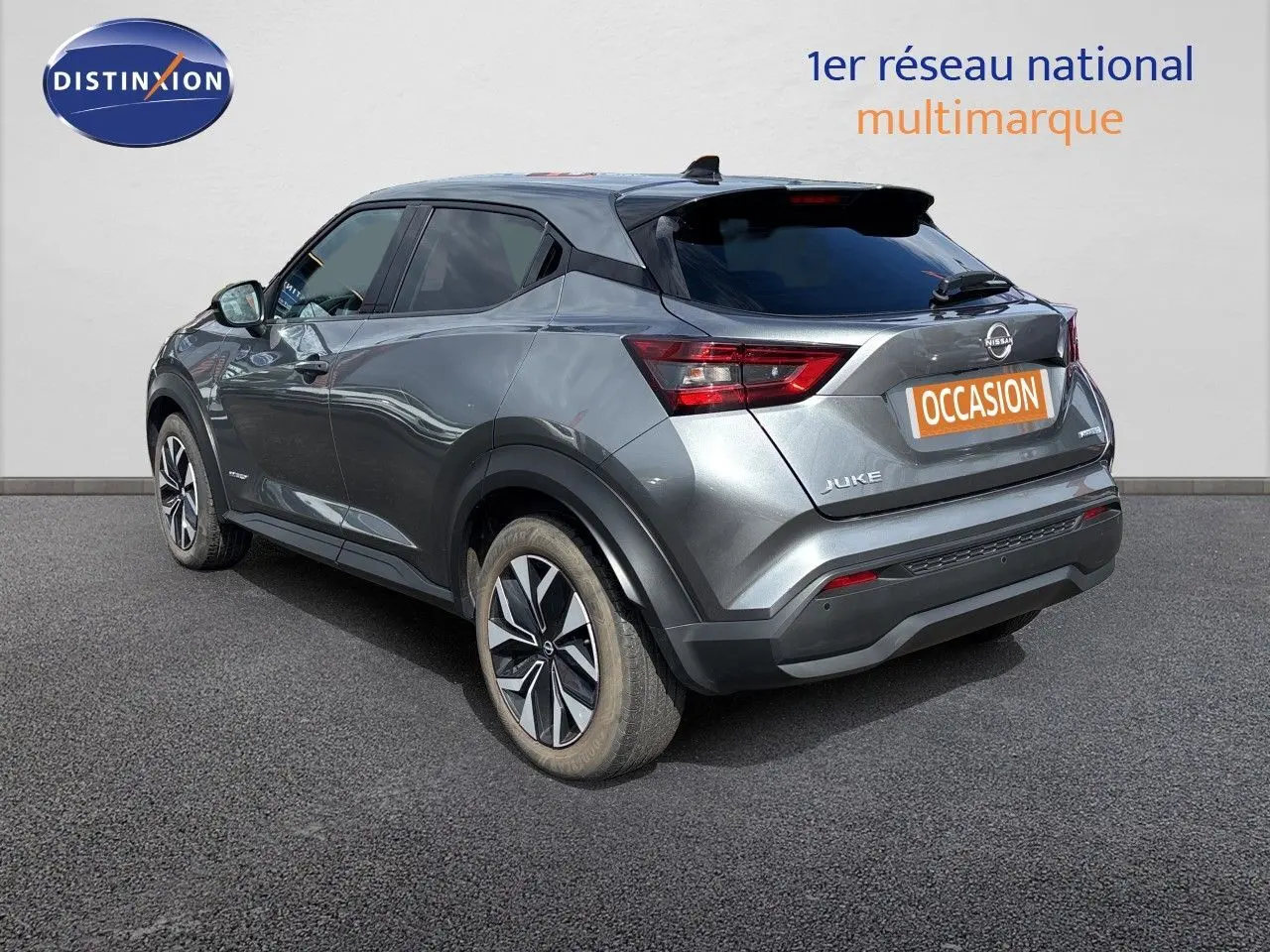 Nissan Juke Hybrid gris squale métal vu de profil côté gauche, avec jantes alliage et lignes dynamiques marquées.