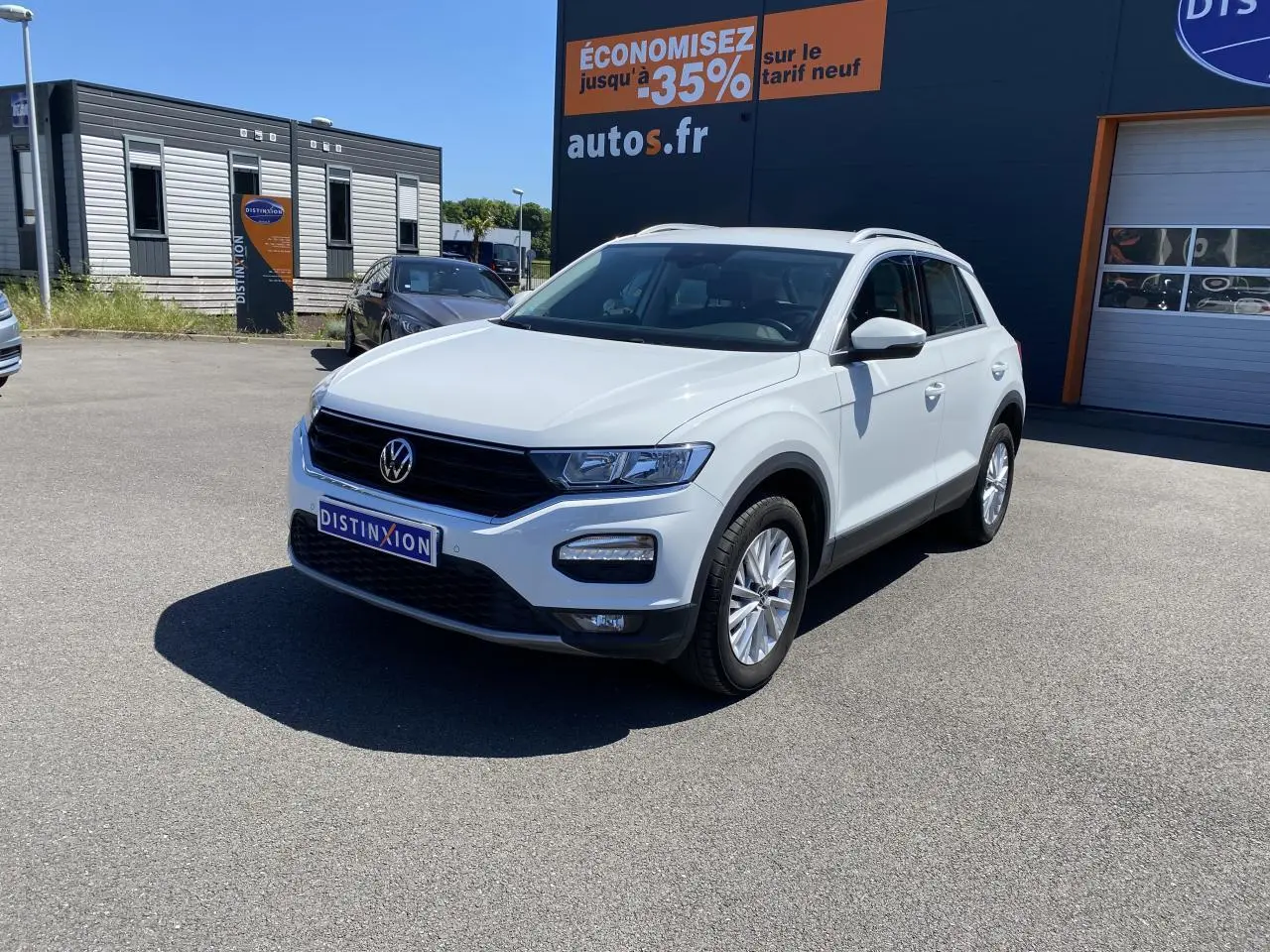 Volkswagen T-Roc blanc pur en 3/4 avant droit, avec calandre noire et jantes alliage visibles sur parking extérieur.