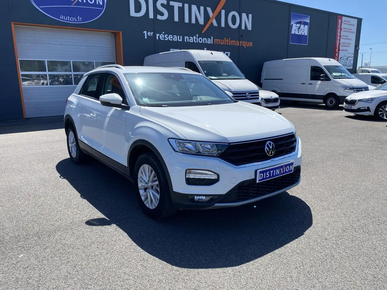 Volkswagen T-Roc blanc pur vu en 3/4 avant droit sur parking devant un bâtiment Distinxion.