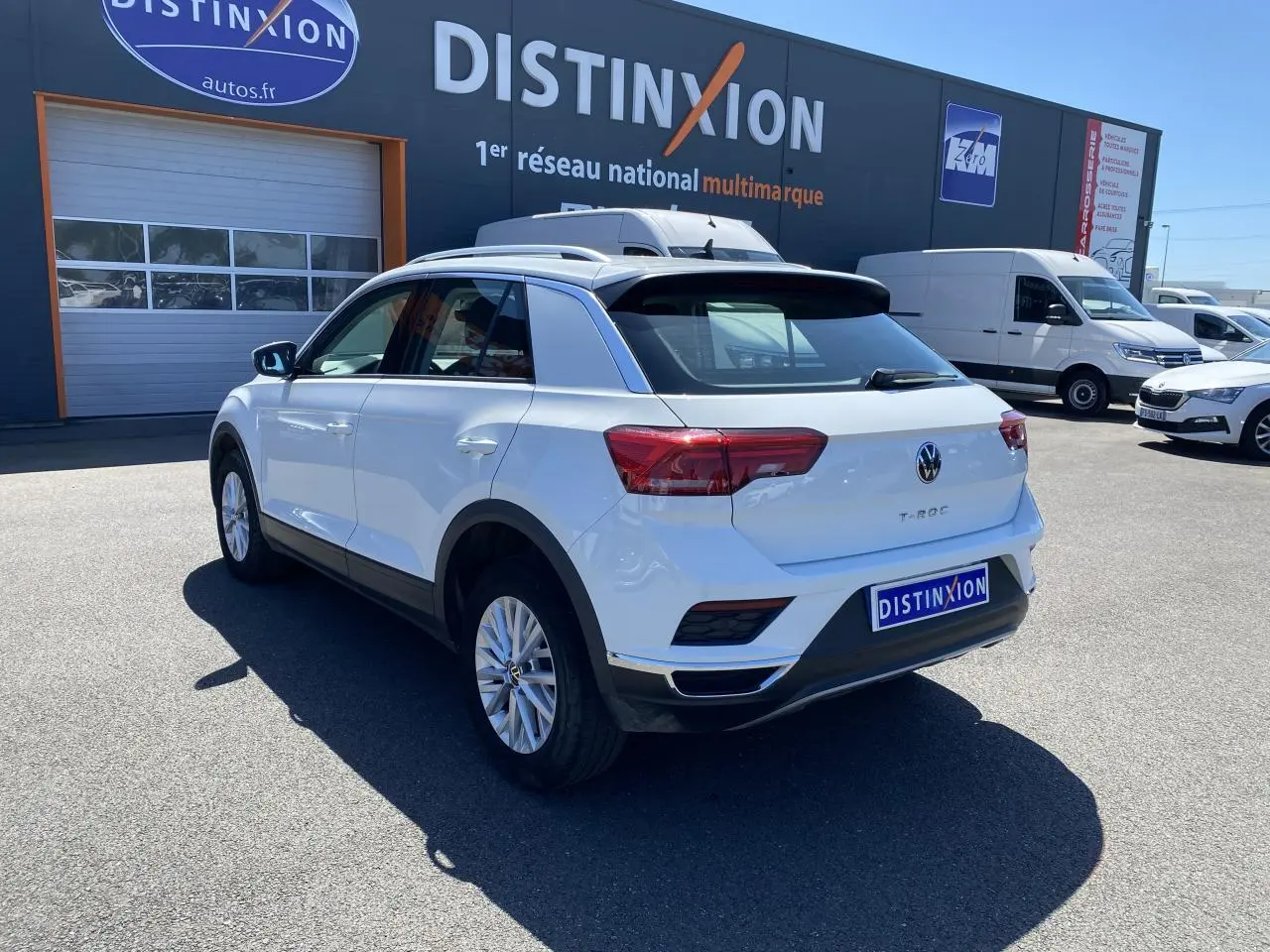 Volkswagen T-Roc blanc pur vu en 3/4 arrière droit, stationné devant un bâtiment avec logo Distinxion.