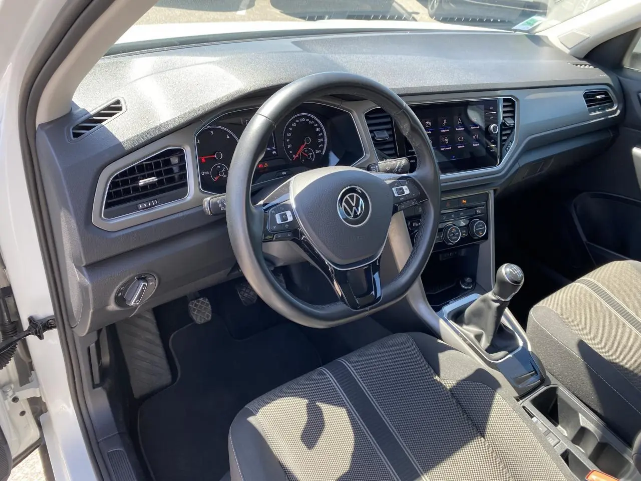 Vue intérieure côté conducteur du Volkswagen T-Roc blanc pur 2021, volant cuir et levier de vitesse manuel visibles.
