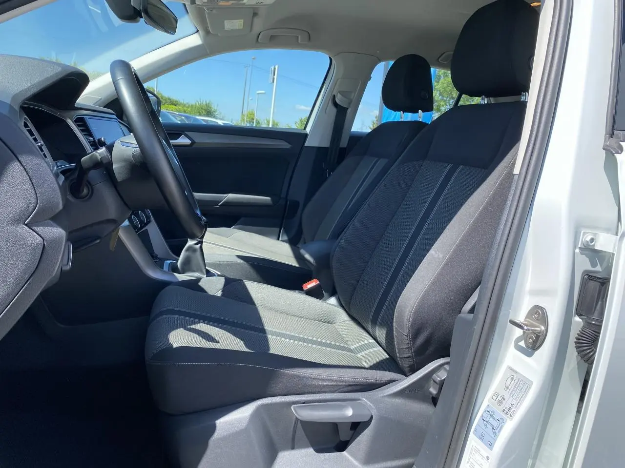 Intérieur côté conducteur d'un Volkswagen T-Roc blanc pur 2021, sièges noirs avec accoudoir central et volant multifonction.