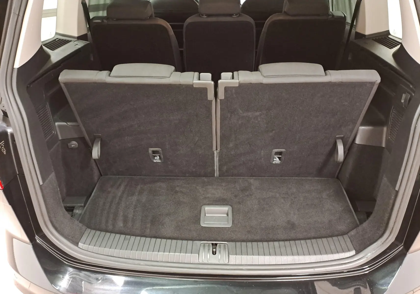 Vue arrière du coffre ouvert du Volkswagen Touran 2025 noir Grenadille, montrant la troisième rangée de sièges relevée.