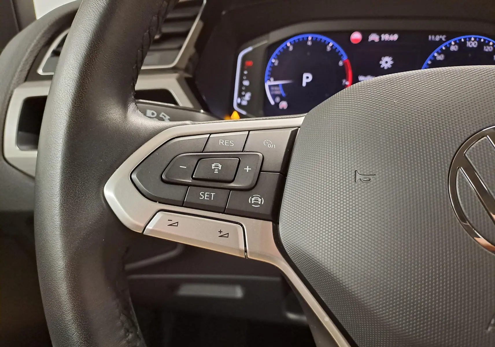 Gros plan sur le volant noir du Volkswagen Touran 2025, avec commandes intégrées et tableau de bord numérique en arrière-plan.