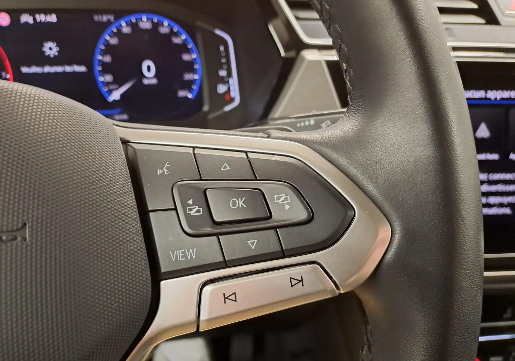 Gros plan sur les commandes multifonctions à droite du volant noir du Volkswagen Touran 2025, tableau de bord numérique en arrière-plan.