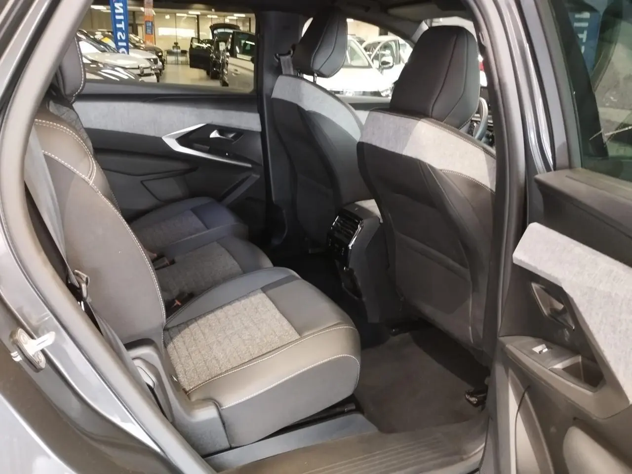 Vue intérieure arrière côté gauche du Peugeot 5008 gris titanium, mettant en valeur les sièges tissu et cuir avec surpiqûres blanches.