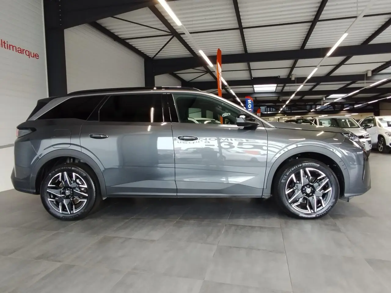 Peugeot 5008 gris titanium vue de profil côté gauche en intérieur avec jantes alliage 19 pouces noires.