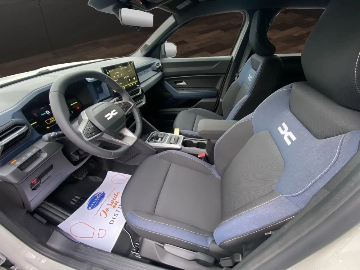 Intérieur du Dacia Duster Journey Hybrid 140 vu côté conducteur, sièges tissu noir et bleu avec logo blanc.