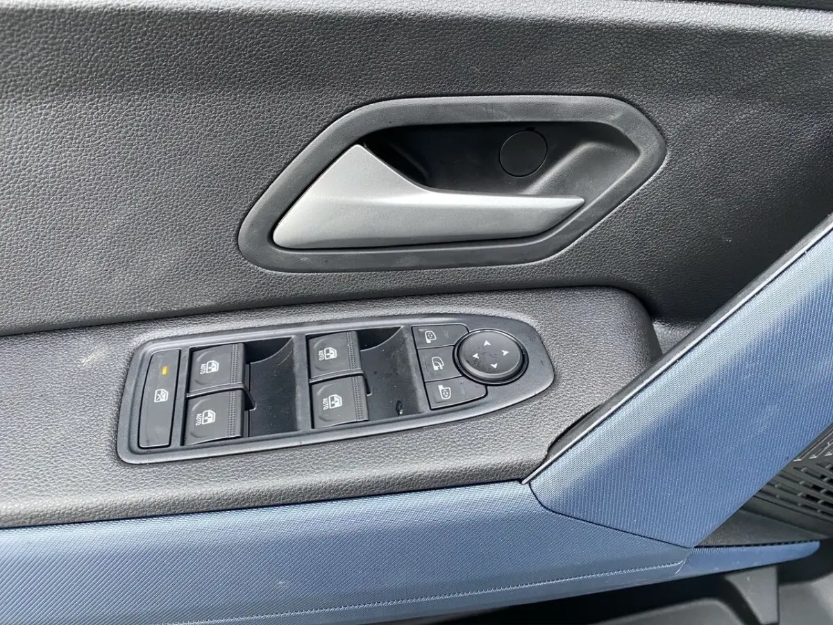 Détail des commandes de lève-vitres et rétroviseurs sur la portière côté conducteur d'un Dacia Duster beige.