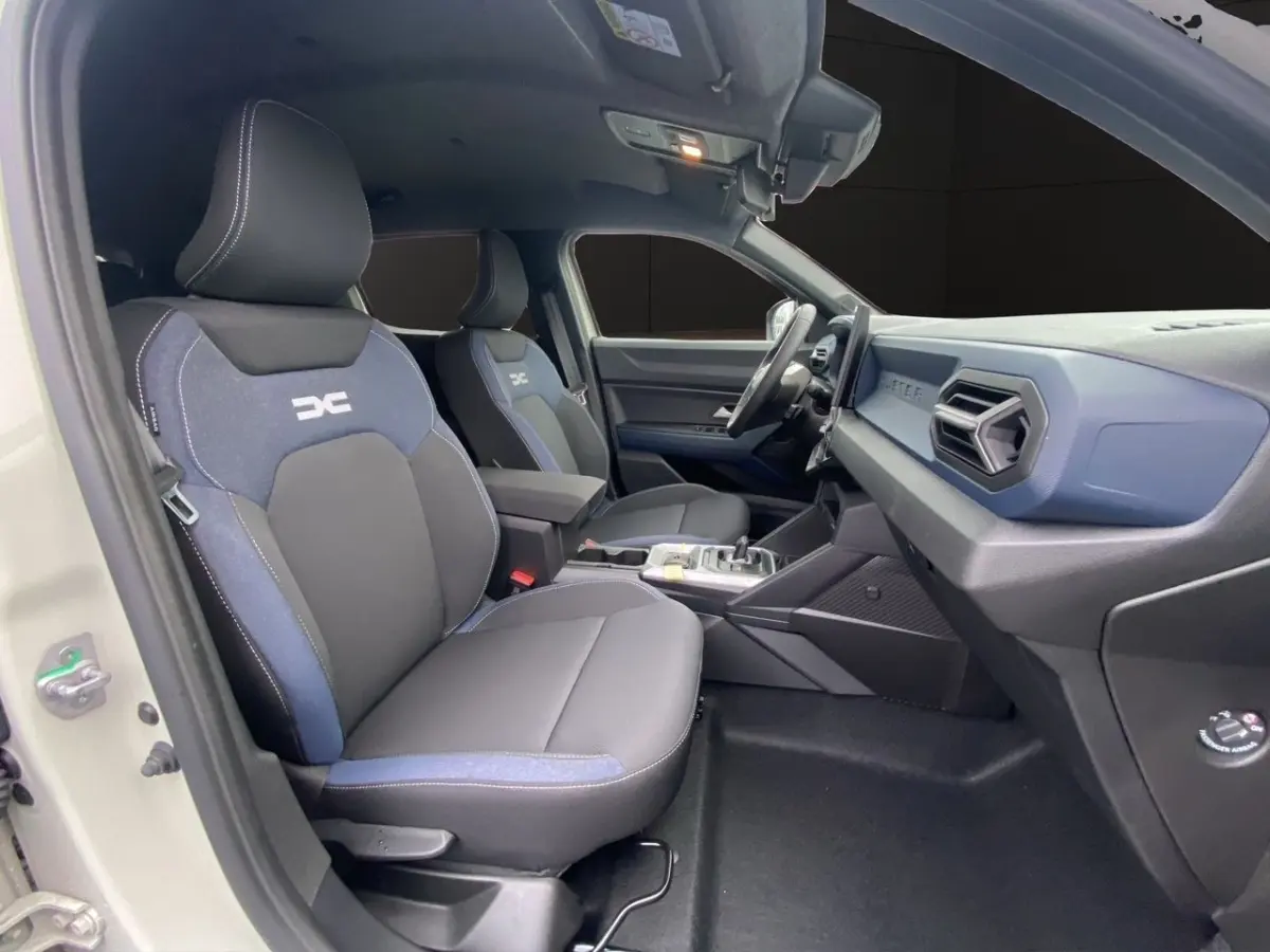Vue intérieure côté conducteur du Dacia Duster beige 2025, sièges tissu noir et bleu avec logo DC brodé.