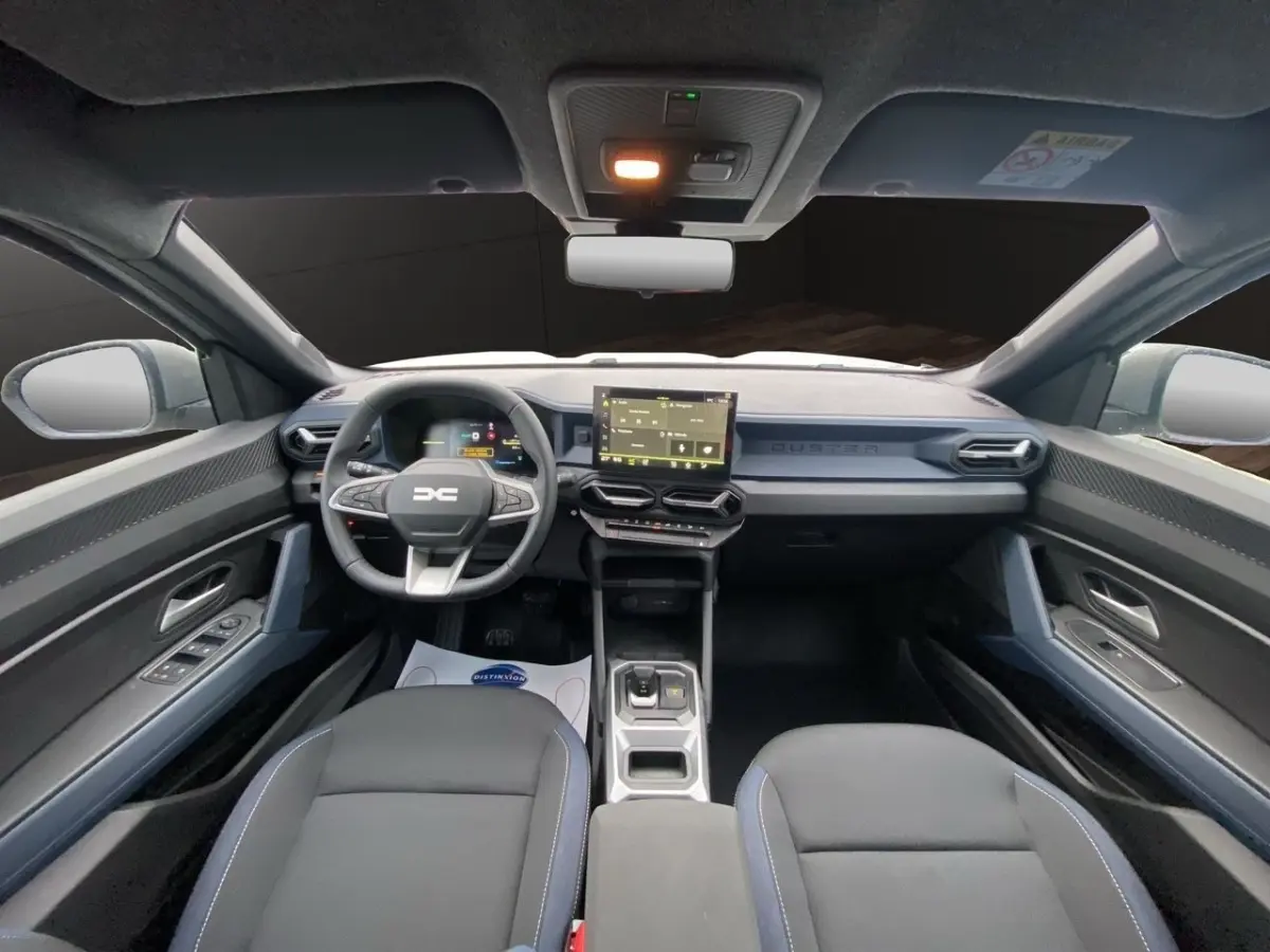 Vue intérieure avant du Dacia Duster Journey Hybrid 140, tableau de bord moderne avec écran tactile central et volant multifonctions.