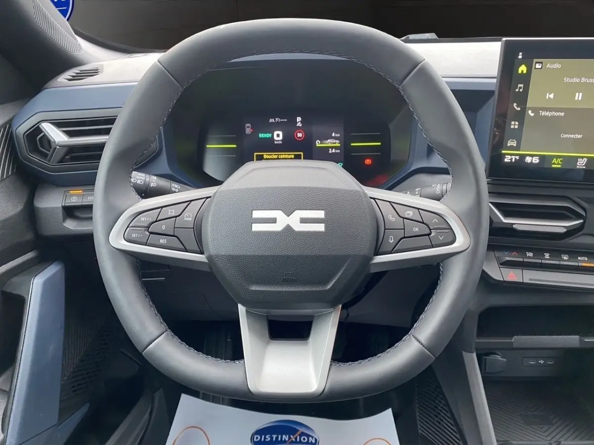 Vue intérieure centrée sur le volant cuir noir du Dacia Duster Journey Hybrid 140 avec tableau de bord digital et écran tactile.