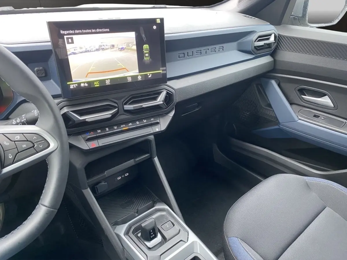Vue intérieure côté passager du tableau de bord et console centrale du Dacia Duster beige avec écran tactile et volant multifonctions.