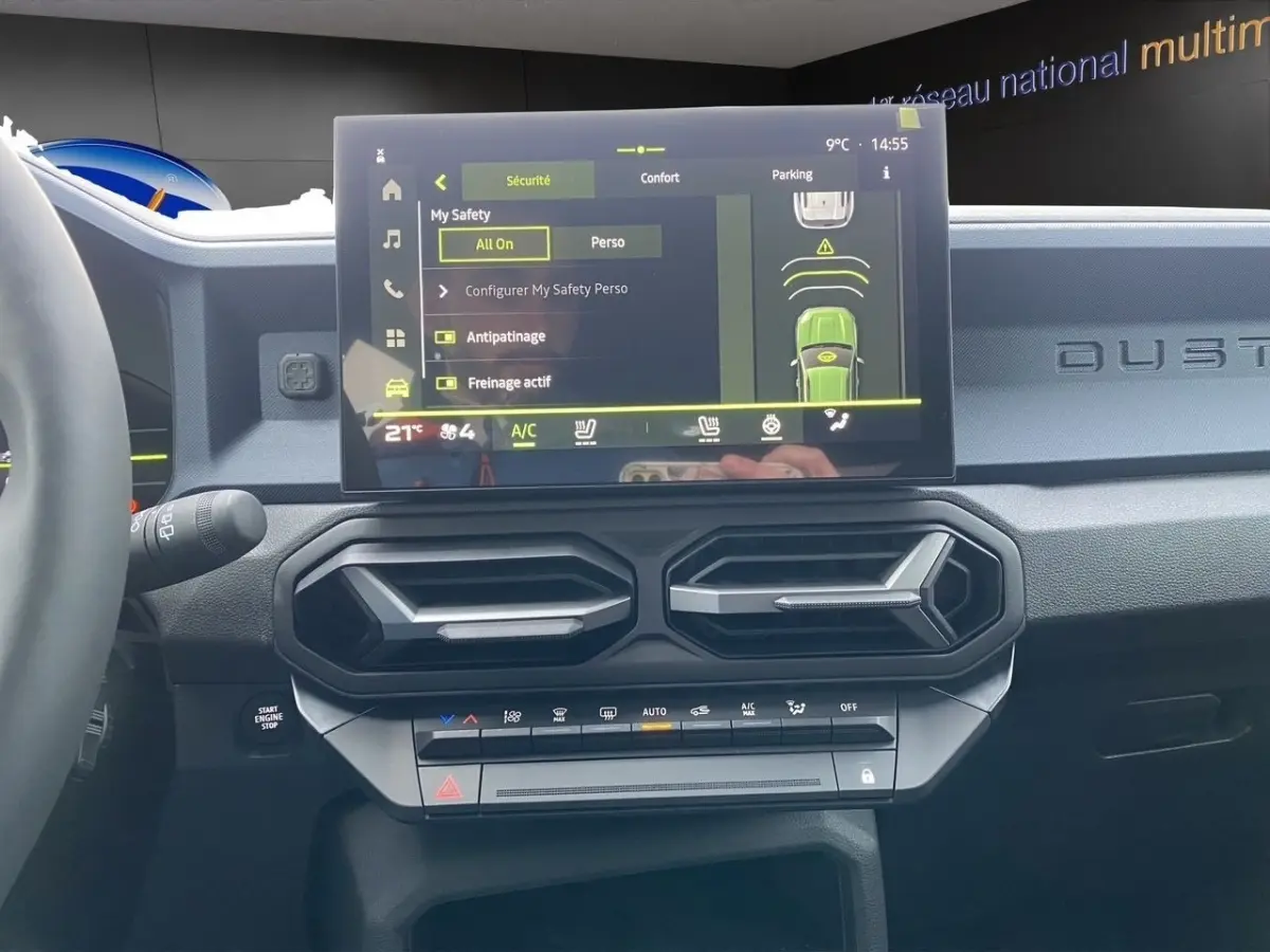 Vue intérieure du tableau de bord du Dacia Duster beige 2025, avec écran tactile central et commandes climatisation.