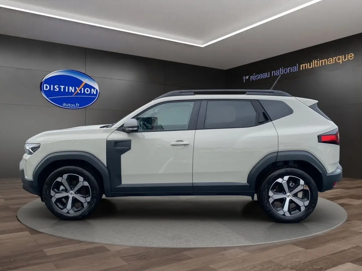 Vue de profil côté gauche du Dacia Duster beige 2025 avec jantes alliage et protections noires sur les passages de roue.