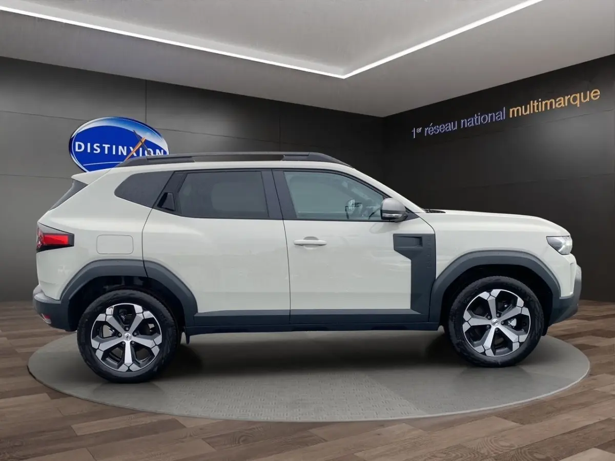 Vue latérale droite du Dacia Duster beige 2025 avec jantes alliage et protections noires contrastantes.