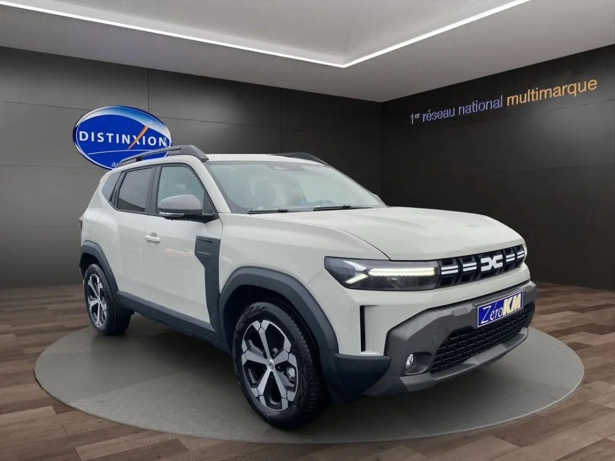 Vue 3/4 avant d'un Dacia Duster beige 2025 avec phares LED et jantes alliage distinctives.