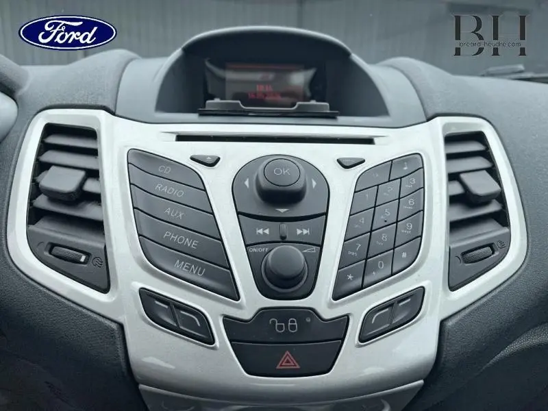 Vue rapprochée de la console centrale gris clair de la Ford Fiesta 2012 avec commandes audio et climatisation.