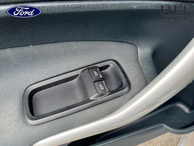 Gros plan sur les commandes des vitres électriques côté gauche de la porte intérieure gris foncé d'une Ford Fiesta gris lunaire 2012.
