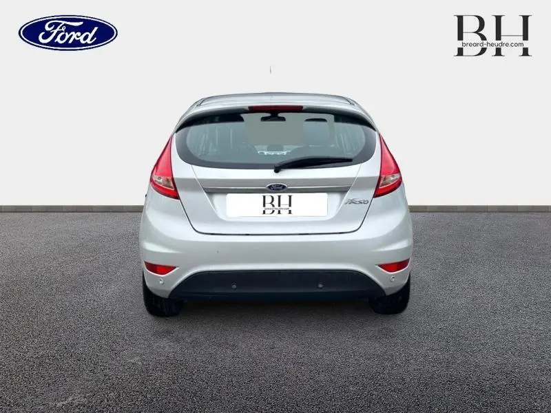 Vue arrière d'une Ford Fiesta gris lunaire de 2012 avec feux arrière rouges et becquet arrière visible.