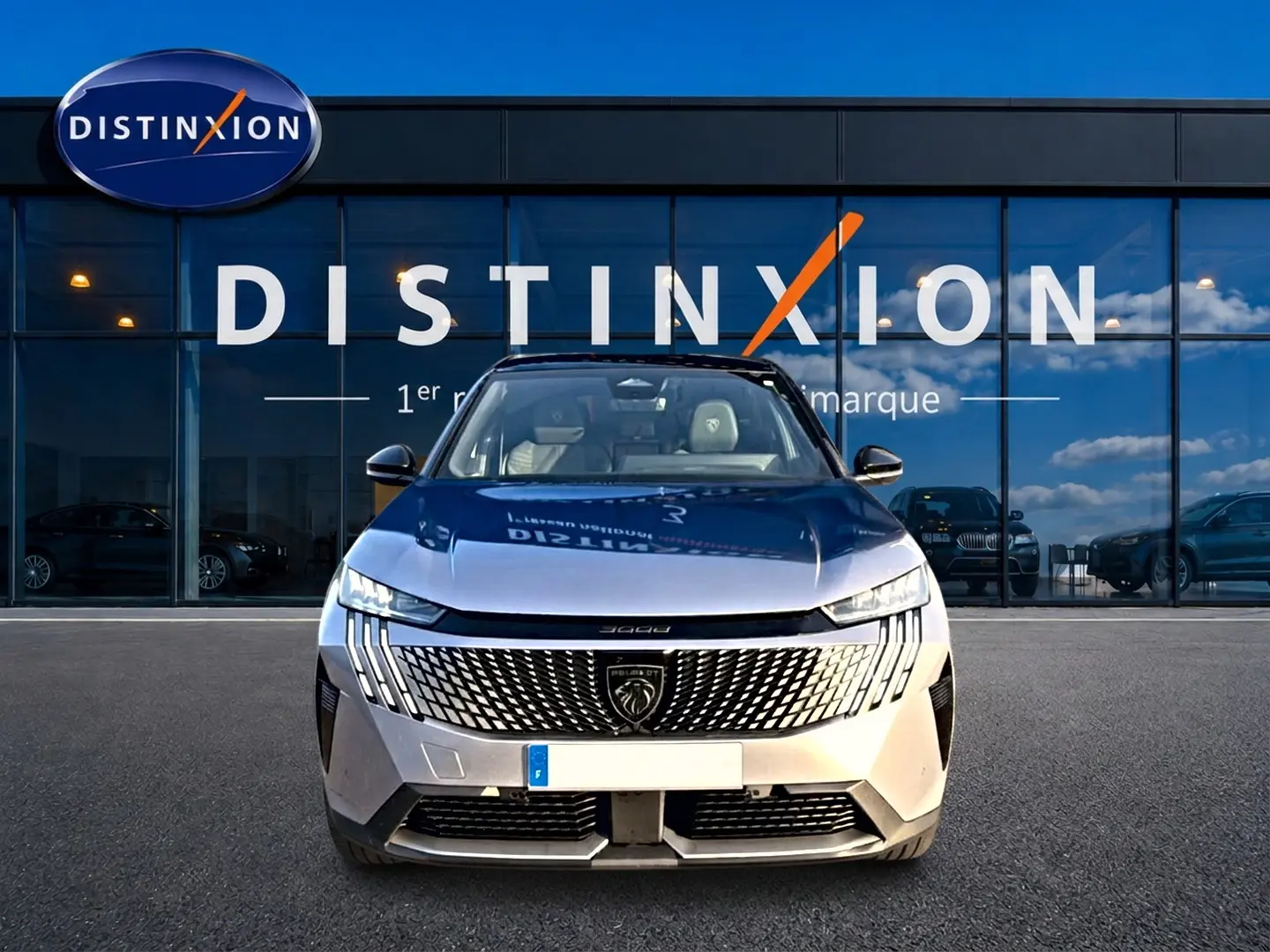 Vue frontale du Peugeot 3008 gris 2025 avec calandre distinctive et phares LED fins devant un showroom Distinxion.