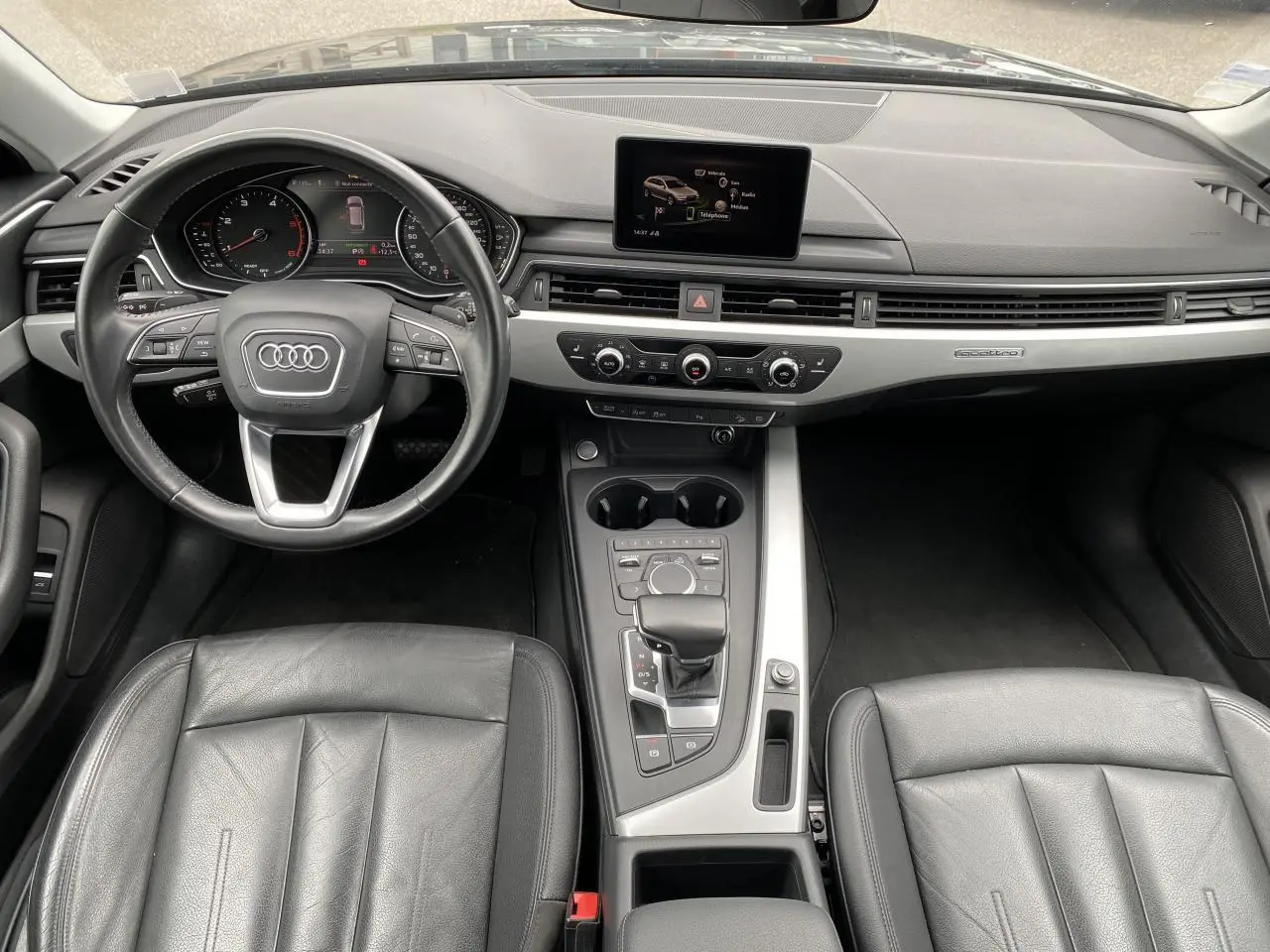 Vue intérieure avant de l'Audi A4 Allroad Quattro 2016 avec tableau de bord noir, écran central et sellerie cuir Milano noire.