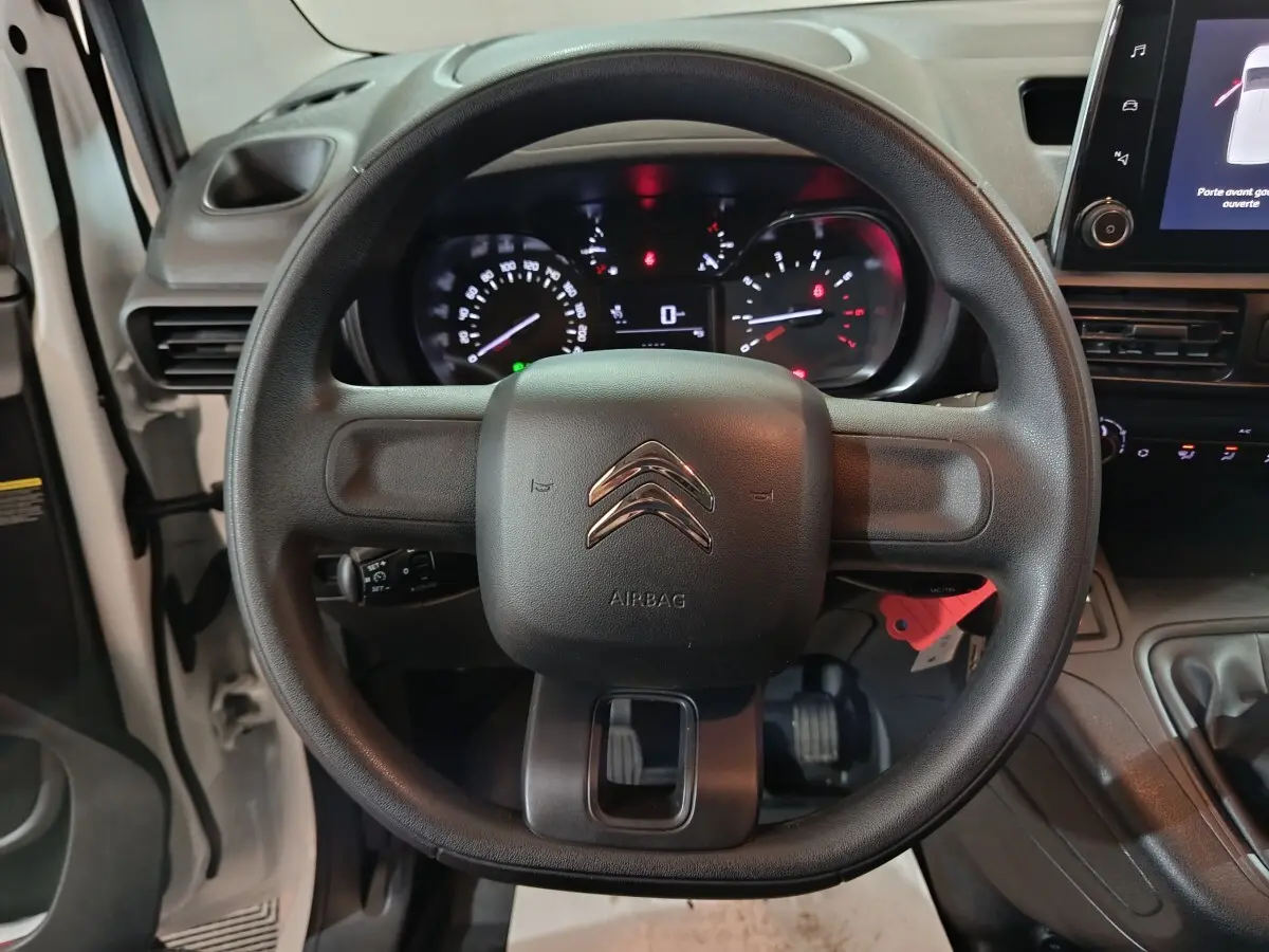 Vue intérieure centrée sur le volant noir du Citroën Berlingo blanc avec tableau de bord et écran tactile visible.