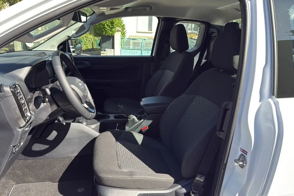 Vue intérieure côté conducteur du Ford Ranger blanc glacier 2025, montrant sièges noirs et volant multifonctions cuir.