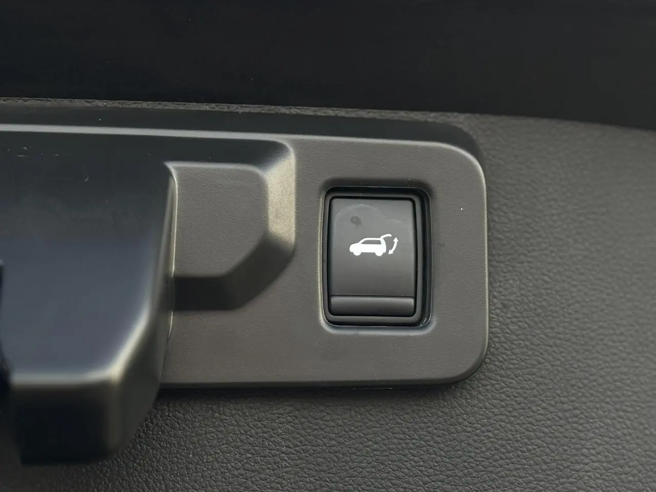 Gros plan sur le bouton d'ouverture du hayon mains libres dans l'habitacle du Renault Symbioz noir étoilé.