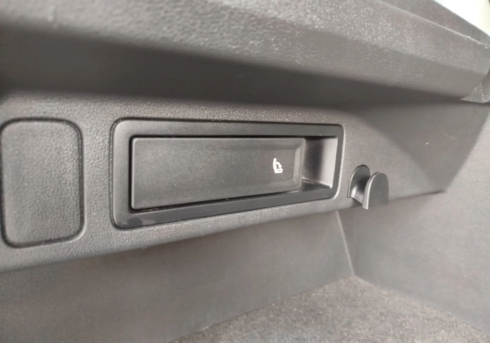 Détail du coffre du Volkswagen Tiguan noir, montrant le levier de rabattement des sièges arrière côté droit.