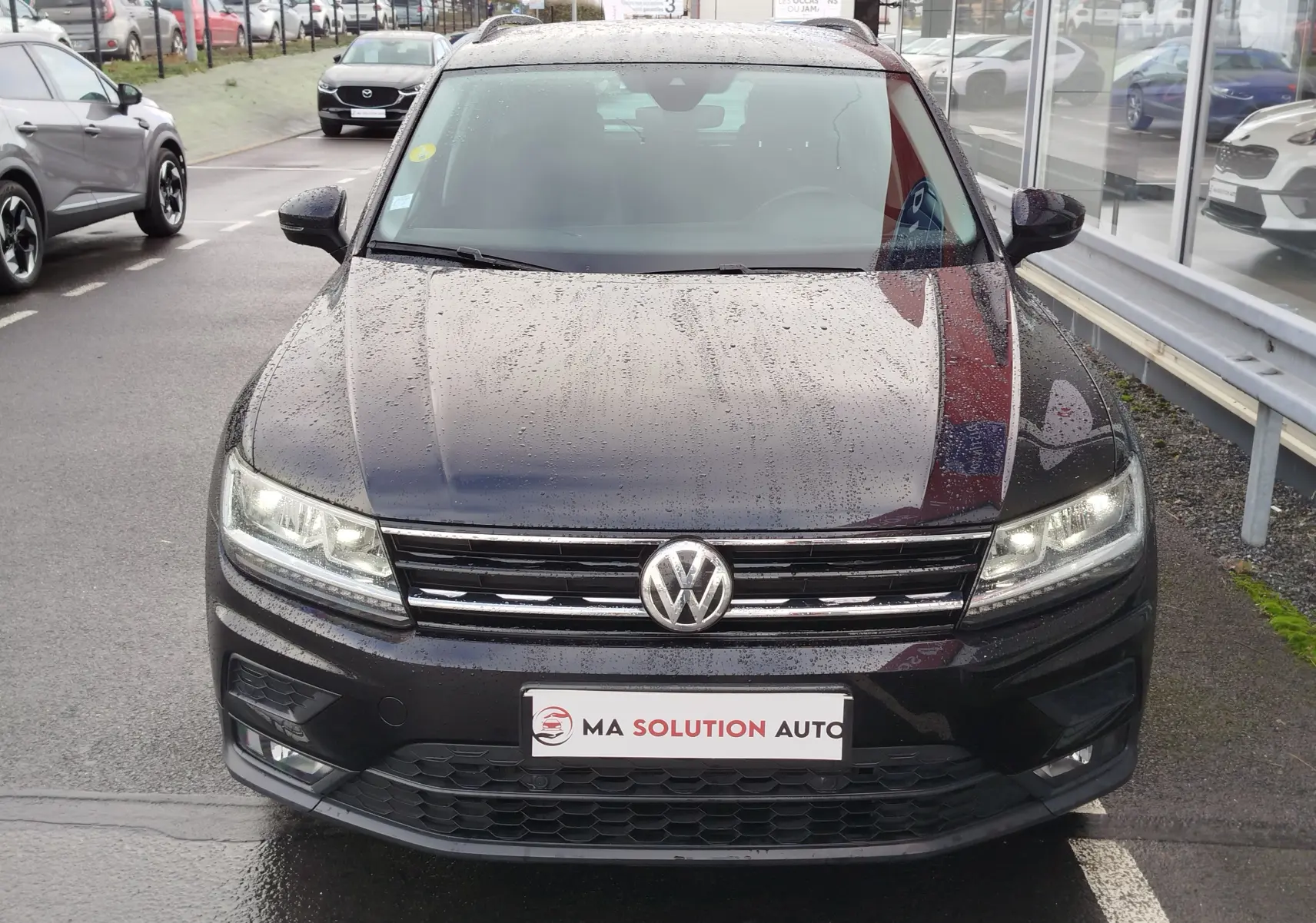 Vue frontale d'un Volkswagen Tiguan noir intense nacré 2019 avec phares allumés et calandre chromée.