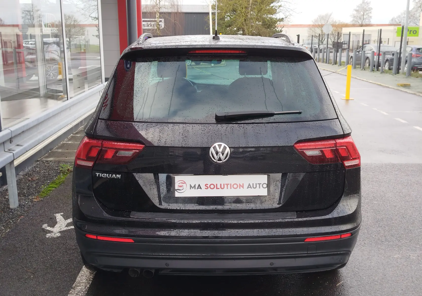 Vue arrière d'un Volkswagen Tiguan noir intense nacré 2019 avec feux arrière LED et logo VW visible sous la pluie.