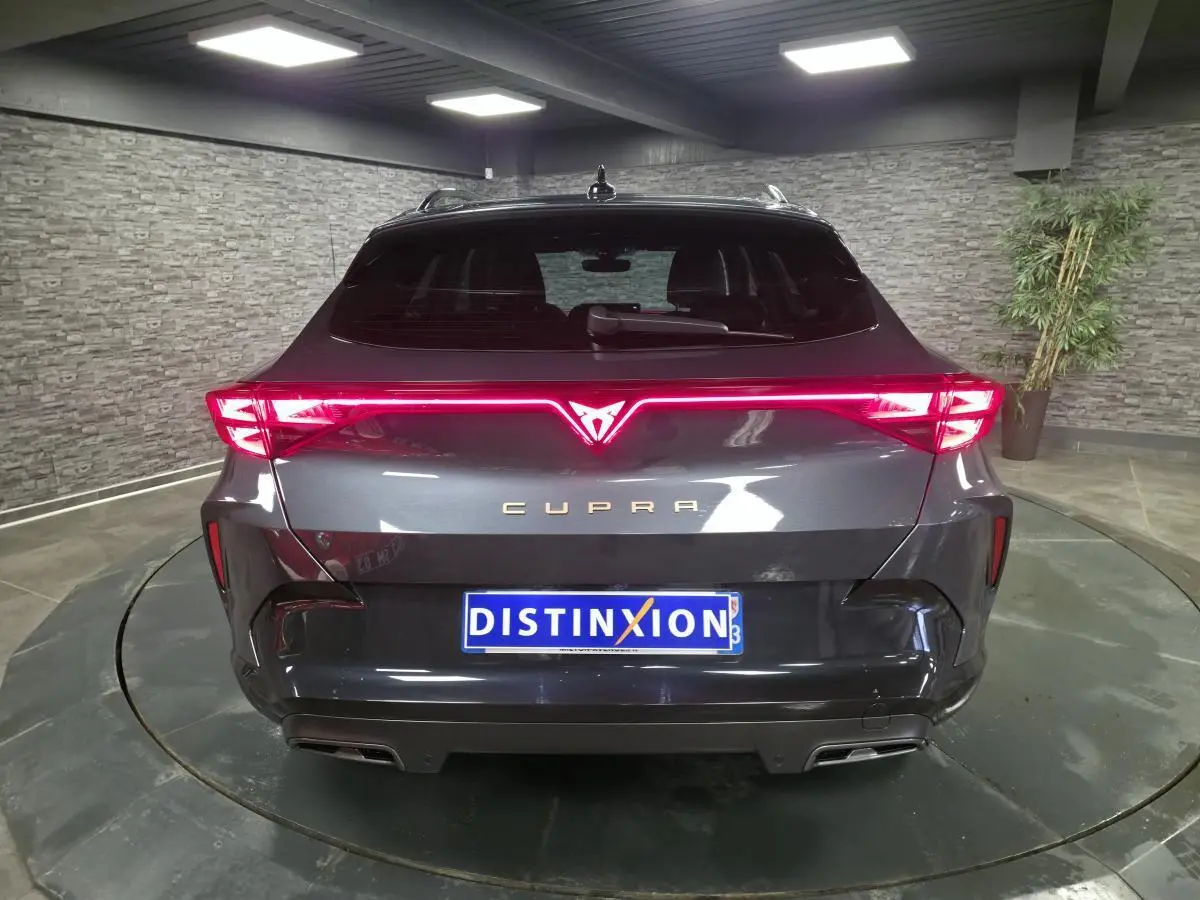 Vue arrière d'une CUPRA Formentor gris métallisé avec bandeau lumineux arrière Tri-LED et double sortie d'échappement noire.
