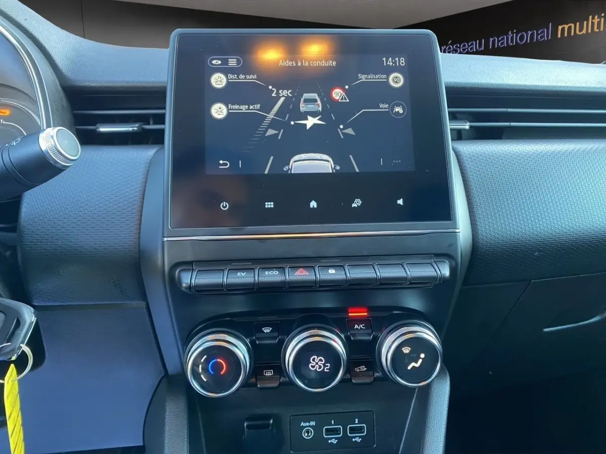 Vue rapprochée du tableau de bord central de la Renault Clio Business E-TECH 140, écran tactile et commandes climatisation visibles.